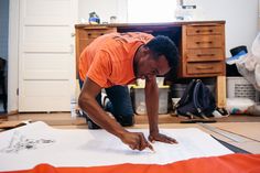 a man in an orange shirt is looking at something on the floor with his hands