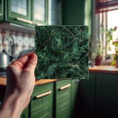 a person holding up a piece of green marble in their hand, near a kitchen counter