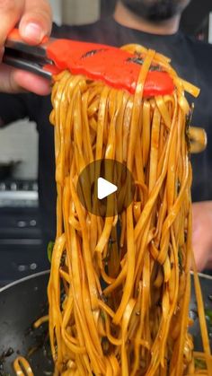 someone is holding chopsticks over noodles in a wok with sauce on top