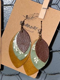 two pairs of brown and green leather earrings hanging from a metal hook on a wire fence