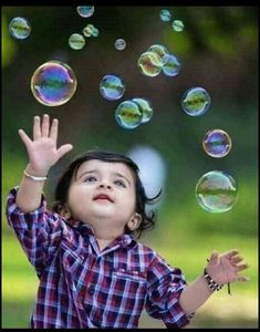 a little boy that is standing in the grass with soap bubbles flying around him and looking up