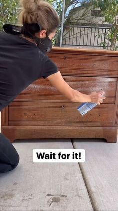 a woman in black shirt waxing wooden furniture with blue paint on the floor and words wait for it