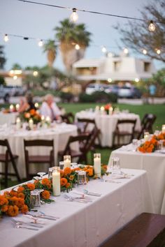 an outdoor dining area with tables and chairs covered in white tablecloths, orange flowers and candles