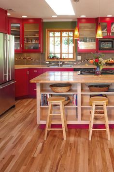 a kitchen with red cabinets and wooden floors, two stools at the center of the island