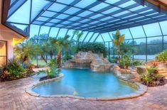 an indoor swimming pool surrounded by palm trees and other greenery, with a waterfall in the center