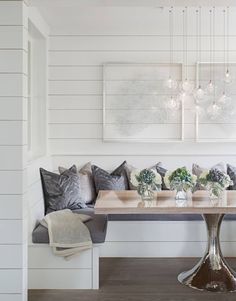 a dining room table and bench with flowers in vases on the end, surrounded by white paneling