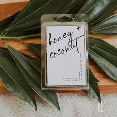 a package of honey and coconut on top of a wooden cutting board next to green leaves