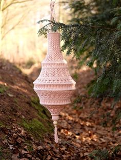 a pink macrame hanging from a tree in the woods with leaves on the ground