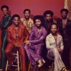 a group of men sitting next to each other in front of a red wall and gold curtain