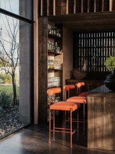 four orange chairs sitting in front of a wooden shelf filled with bottles and jars next to a window