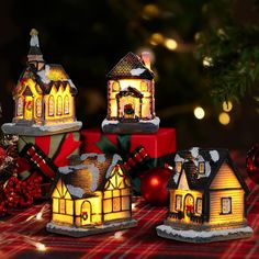 three lit up houses sitting on top of a table next to christmas balls and ornaments