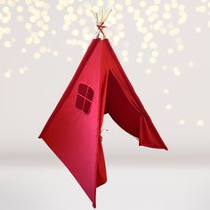 an ornament shaped like a red tent hanging from a string with lights in the background