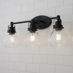 three clear glass globe lights hang on the wall above a white tiled bathroom countertop