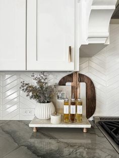 a kitchen with white cabinets and marble countertops is pictured in this image, there are two bottles of alcohol on the tray