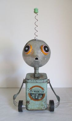 an old metal robot with eyes and nose sitting on top of a table next to a white wall