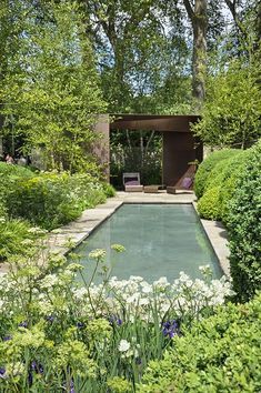 an outdoor pool surrounded by trees and bushes in the middle of a garden with white flowers