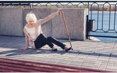 a woman with white hair sitting on the ground next to a wall and holding a cane