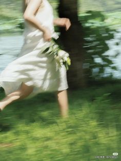 a blurry photo of a woman in a white dress running with flowers on her hand