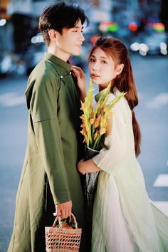 a young man and woman standing next to each other on the street with flowers in their hands