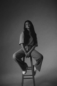 a black and white photo of a woman sitting on top of a wooden stool with her legs crossed