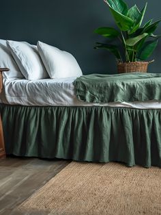 a bed with a green bedspread next to a potted plant on top of it