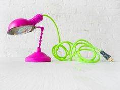 a pink and green desk lamp sitting on top of a white table next to a charger