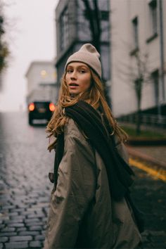 a woman walking down the street with a scarf around her neck and a hat on