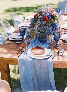 a wooden table topped with plates and vases covered in blue cloth draped over it