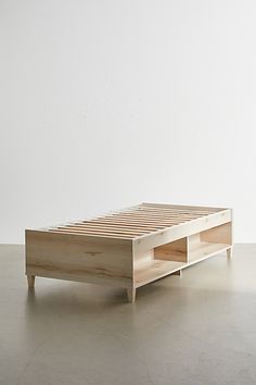 a wooden bed frame sitting on top of a cement floor next to a white wall