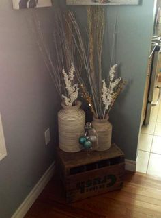 two vases with dried flowers are sitting on a crate in front of a wall