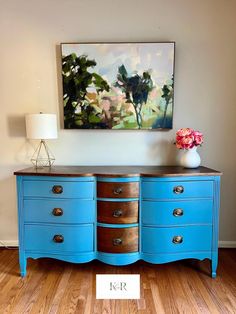 a blue dresser with two drawers and a painting on the wall