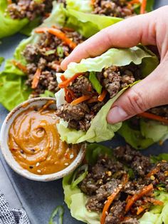 a person dipping sauce onto lettuce wraps with carrots and other toppings