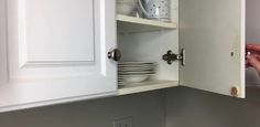 a kitchen cabinet with dishes in it and someone holding the door open to reveal plates