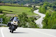 a man riding a motorcycle down a curvy road next to a lush green hillside