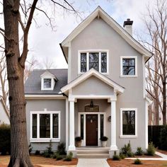 a gray house with white trim and two large trees in front of the entrance to it