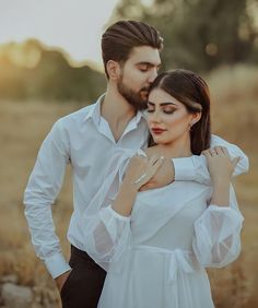 a man and woman are standing close together in the middle of a field with grass