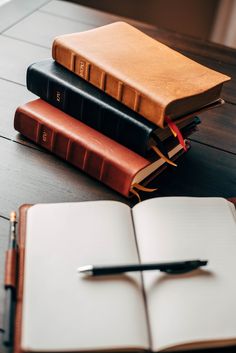 three books and a pen are sitting on a table next to an open notebook, which is resting on top of another book