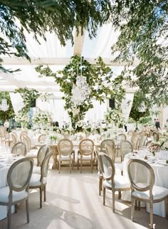 a dining room with tables and chairs covered in white linens, surrounded by greenery