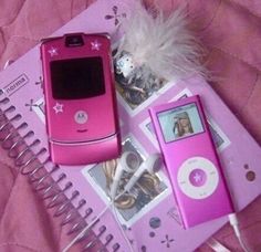 two pink cell phones sitting next to each other on top of a notebook with ear buds