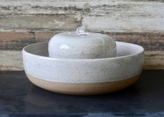 a white bowl with an apple in the center on a black table next to a wooden wall