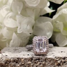 an emerald colored diamond ring sitting on top of a rock next to some white flowers