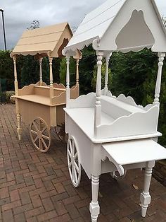 two white wooden carts sitting next to each other on a brick walkway with trees in the background