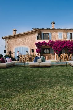 an outdoor living area with couches, tables and flowers on the lawn in front of a house