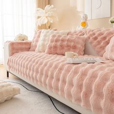 a living room with a couch covered in pink fluffy blankets and pillows, next to a window