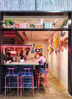 two people sitting at a table in front of a wall with colorful artwork on it