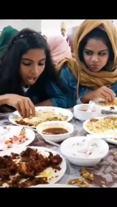 two women sitting at a table with plates of food in front of them and one woman looking down