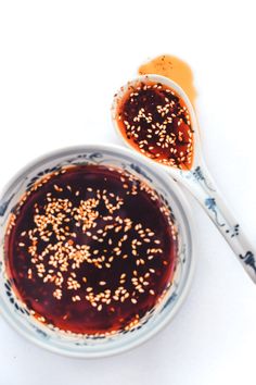 two spoons are next to a bowl filled with sauce and sesame seed sprinkles