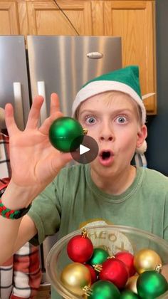 a young boy wearing a santa hat holding up christmas ornaments in front of his face