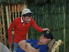 a man in red shirt laying on top of a chair next to another man wearing a hat