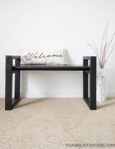 a black bench with a welcome sign on it in front of a white wall and two vases